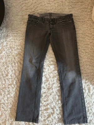 Lågmidjade jeans - Säljer ett par lågmidjade grå jeans med raka ben och snygga slitningar. Materialet är klassisk denim och färgen är tvättad grå med ljusare partier och har unika detaljer. Perfekta för en avslappnad och trendig look. W28, Midjemått 41cm, passar bra i längd på mig som är 165cm, passar även kortare. 
