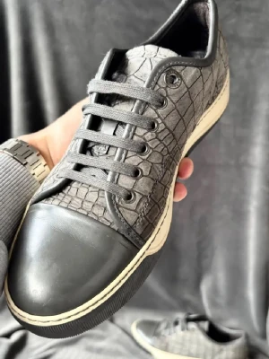 Lanvins med krokodilstruktur - Unika grå sneakers med krokodilpräglat mönster och tåhätta i gummi. Skorna har grå snörning, vit sula och detaljer i svart. Materialet ser ut som konstläder med en cool textur som sticker ut. Perfekta för dig som vill ha något annorlunda till din outfit. Storlek 40-41