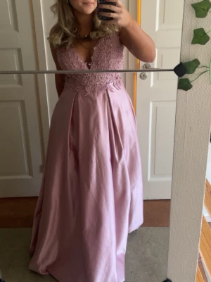 Ljusrosa balklänning med spets🩷 - Säljer en elegant ljusrosa balklänning med v-ringad spetsliv och vid kjol i satinliknande material. Klänningen har breda axelband och öppen rygg, perfekt för bal eller student. Romantisk look med fina spetsdetaljer upptill och slät kjol nedtill. Använd en gång! Passar perfekt för dig som är runt 170 lång eller 165 med klackar!!  Står L på lappen men skulle säga att den passar som en M då det är min vanliga storlek!⭐️