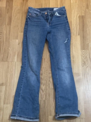 Blå bootcut jeans från vero Moda - Säljer ett par blå bootcut jeans från vero mods  med klassisk femficksmodell och lätt slitning på ena benet. Jeansen har normalhög midja och är tillverkade i denim med lite stretch. Perfekta för en avslappnad och trendig look.