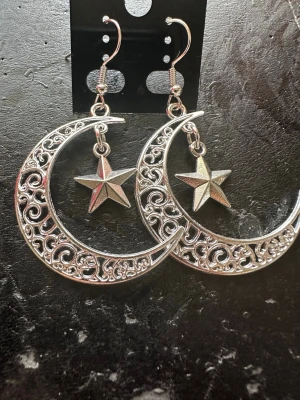 Silvriga örhängen med måne och stjärna - Unika örhängen i silverfärgad metall med stora halvmånar i filigrandesign och dinglande stjärnor i mitten. Snyggt statement-smycke med cool och mystisk vibe. Perfekta för dig som gillar detaljer och vill sticka ut.