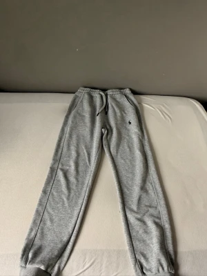 Grå mjukisbyxor från Polo Ralph Lauren - Snygga grå mjukisbyxor från Polo Ralph Lauren med dragsko i midjan och resår vid bensluten. Klassisk logga broderad på benet. Tillverkade i mjukt och bekvämt material, perfekta för chill dagar eller när du vill vara extra comfy.