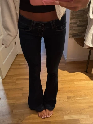 Mörkblå bootcut hollister jeans  - Säljer ett par mörkblå bootcut jeans med vita kontrastsömmar och låg midja. Jeansen har klassiska fem fickor och utsvängda ben. Materialet är denim med stretch för skön passform. Perfekta för en trendig och avslappnad look.