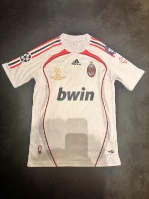 AC Milan bortatröja Maldini #3 - Säljer en vit AC Milan bortatröja från Adidas med Maldini och nummer 3 på ryggen. Tröjan har röda och svarta detaljer, Champions League-märke på ärmen och Bwin som sponsor på bröstet. Tillverkad i lätt och ventilerande material, perfekt för fotboll eller samling.