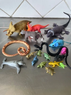 Samling plastdjur och dinosaurier - Säljer en samling med plastdjur och dinosaurier i olika färger och former. Innehåller bland annat ödlor, ormar, hund, säl, sköldpadda och flera smådjur. Perfekt för lek eller dekoration. Alla figurer är gjorda i plast och har olika färger som blå, gul, grön, rosa och svart.