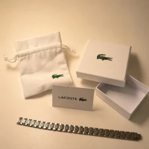 Lacoste armbandslänk i silver - Snygg armbandslänk från Lacoste i silverfärgad metall. Länken har en stilren design med små rektangulära länkar och diskreta Lacoste-loggor. Kommer med original ask och tygpåse med broderad krokodil. Perfekt accessoar för dig som gillar klassisk stil.