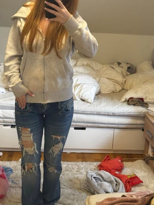 Blå slitna bootcut jeans - Säljer ett par blå bootcut jeans med stora slitningar och hål på båda benen. Jeansen har klassisk femficksdesign och låg midja. Perfekta för en avslappnad och trendig streetstil. Från Ltb i storlek M