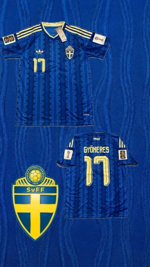 Äkta Sverige Vm tröja - GYÖKERES 17 + VM PATCH - Säljer en blå fotbollströja från Adidas med Sveriges landslagsemblem på bröstet och gula detaljer. Tröjan har nummer 17 och namnet Gyökeres på ryggen, samt gula ränder på axlarna och unikt mönster över hela tyget. Perfekt för dig som älskar fotboll och vill stötta Sverige!