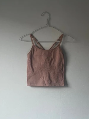 Rosa ribbad träningstopp med smala bandSnygg randig linnetopp med tunna axelband i vitt och grått. Toppen har en enkel och stilren design, perfekt för varma dagar. Materialet känns mjukt och lätt mot huden. - Säljer en rosa ribbad träningstopp med smala axelband och croppad passform. Toppen har ett diskret randigt mönster 