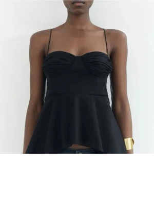 Svart peplum linnetopp med tunna band - Snygg svart linnetopp med tunna axelband och peplumskuren nederdel. Toppen har en figurnära passform upptill och lätt rynkade kupor för en trendig look. Perfekt att styla med jeans eller kjol för en cool outfit.