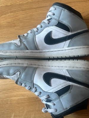 Nike Dunk High grå och vita sneakers - Nike Dunk High sneakers i grått och vitt med svart Swoosh på sidan. Klassisk hög modell med snörning och vadderad krage. Innersulan borttagen! Finns ett litet hål/punka på ovansidan därav det extrem låga priset. Möts helst upp i Malmö och tar swish.