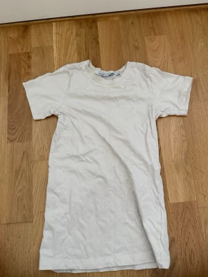 Vit basic t-shirt klänning från 157 - En enkel vit t-shirt klänning från 157 med rund hals och korta ärmar. Tillverkad i mjuk bomull, perfekt för en clean och avslappnad stil. Passar till det mesta och är ett måste i garderoben.