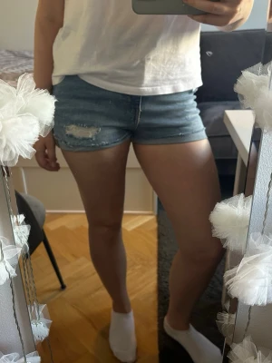 Blå jeansshorts med slitningar - Ett par fina högmidjade blå jeansshorts med slitna detaljer och uppvikta på nederkanten🙌. Passar till det mesta.