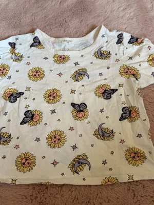 Vit t-shirt med sol- och måntryck - Vit t-shirt från Good Vibes Only med färgglatt tryck av solar, månar, fjärilar och små stjärnor etc. T-shirten är lite croppad. Strl står ej men gissar på Xs, S.  Kan användas ute eller som pyjamas.