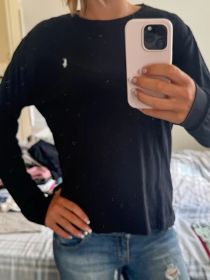 Svart långärmad topp från Polo Ralph Lauren - Klassisk svart långärmad topp från Polo Ralph Lauren med rund halsringning och den ikoniska broderade loggan på bröstet. Tillverkad i mjuk bomull som känns skön mot huden. Perfekt basplagg till garderoben.