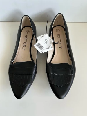 HELT NYA Svarta loafers med fransdetalj Esmara - storlek 39 - Helt nya svarta ballerinaskor / loafers från Esmara i storlek 39. Tidlös modell med spetsig tå och dekorativa fransar framtill. Platt bekväm sula. Veganskt konstläder. Lika fina till byxor som till kjol. Helt nya, oanvända med etikett. 