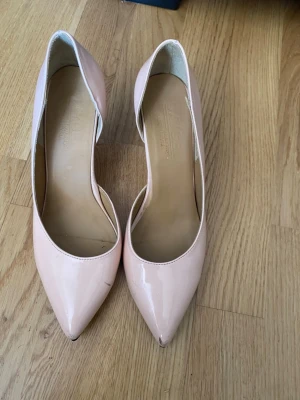 Ljusa rosa lackade pumps - Snygga pumps i ljusrosa lack med spetsig tå och klassisk klack. Skorna har en elegant och stilren design som passar till många olika outfits. Tillverkade i ett glansigt material som ger en trendig look.