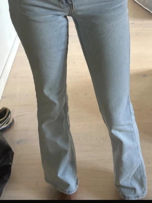 Ljusblå bootcut jeans med fickdetalj - Säljer ett par ljusblå bootcut jeans med snygg fickdetalj bak och knapp. Jeansen har klassisk femficksmodell och är tillverkade i mjukt denimtyg med lätt stretch. Perfekta för dig som gillar en avslappnad men trendig look.