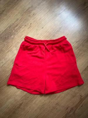 Röda mjuka shorts med snörning - Snygga röda shorts i mjukt material med elastisk midja och snörning framtill. Perfekta för chill dagar eller träning. Klassisk passform och enkel design utan extra detaljer.