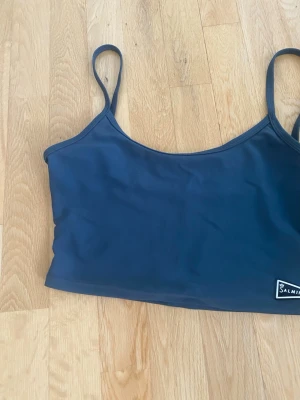 Gråblå linnetopp från Salming - Sportig gråblå linnetopp från Salming med smala axelband och enkel design. Tillverkad i ett stretchigt syntetmaterial som passar perfekt för träning. Liten Salming-logga framtill i vitt och svart.