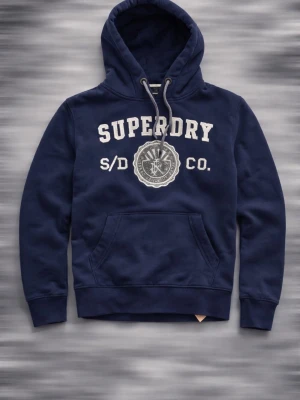 Marinblå hoodie från Superdry - Snygg marinblå hoodie från Superdry med broderad logga och text framtill. Klassisk känguruficka och justerbar huva med grå dragsko. Perfekt för en avslappnad och sportig stil. Mjukt material som känns skönt mot huden. Passar XS bäst 