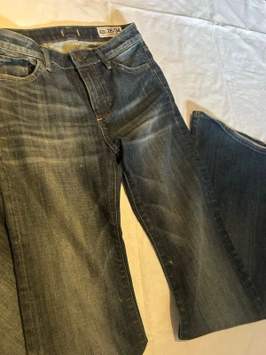 Mörkblå jeans boot cut - Snygga mörkblå jeans från med klassisk femficksmodell och slitna detaljer. Jeansen har raka ben och tydliga kontrastsömmar. Tillverkade i kraftigt denimtyg som ger en cool och avslappnad look.
