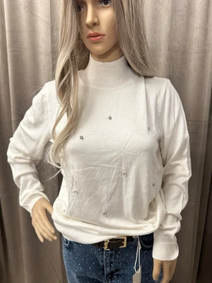 Vit stickad tröja med pärldetaljer M-L - En vit stickad tröja med hög krage och långa ärmar. Tröjan har små pärldetaljer på framsidan som ger en snygg och trendig look. Ribbstickade muddar vid ärmslut och nederkant. Perfekt för dig som gillar stilrena plagg med en twist.