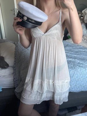 Vit kort sommarklänning - studentklänning  - Söt vit kort klänning med tunna axelband och spetsdetaljer upptill. Klänningen har v-ringning och volangliknande lager nertill. Perfekt till studenten och sommaren. Har lite små vaga fläckar på framsidan 