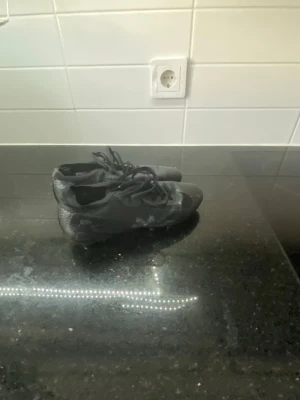 Svarta fotbollsskor med dobbar - Säljer ett par helsvarta fotbollsskor med klassisk snörning och fasta dobbar. Skorna har en sportig design och är tillverkade i syntetmaterial som ger bra grepp på planen. Perfekta för dig som vill ha stilrena och funktionella skor till match eller träning.