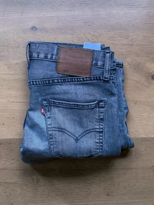 Levi's 501 blå jeans - Klassiska blå Levi's 501 jeans med rak passform och fem fickor. Jeansen har en brun läderpatch bak i midjan och den ikoniska röda Levi's-taggen på bakfickan. Tillverkade i slitstark denim, perfekta för en avslappnad och tidlös stil.