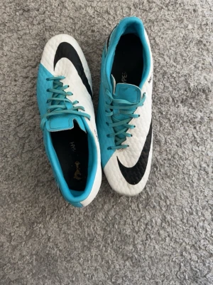 Nike Hypervenom blå/vita fotbollsskor - Snygga Nike Hypervenom fotbollsskor i storlek 45,5 vitt och blått med svarta detaljer och klassisk Nike-logga som säljs för att de är för små. Skorna har snörning och dobbar för bra grepp på planen. Perfekta för dig som vill sticka ut på matchen och satsa på snabbhet och kontroll. De har en liten defekt vid snören men det går såklart att fixa. Pris kan diskuteras!