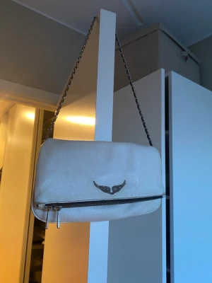 Vit zadig väska - Äkta axelväska från zadig & voltaire. Går att vika banden i kors ” under väskan innan man stänger ” för att förkorta dom, (så jag brukar bära den). Använt en del men fortfarande i bra skick. Har fickor. 🤍pris kan diskuteras