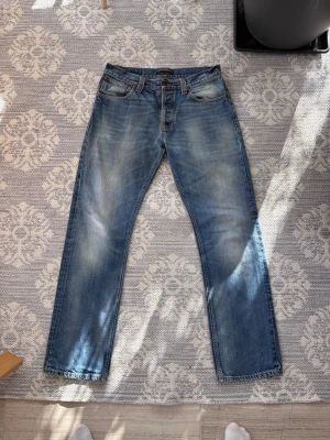 Nudie jeans  - 34/34 riktigt bra skick. Snygga blå jeans från Nudie jeans med raka ben och klassisk femficksdesign. Jeansen har en lätt tvättad look med fades på låren och knäna. Perfekta för en avslappnad stil och tillverkade i bomull.