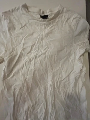 Vit basic t-shirt i bomull - H&M - En klassisk vit t-shirt i mjuk bomull med rund hals och korta ärmar. Perfekt att matcha med jeans eller shorts för en enkel och stilren look.