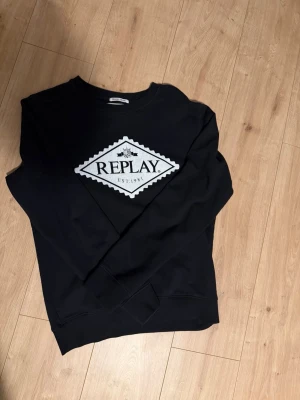 Svart sweatshirt från Replay - Svart sweatshirt från Replay med stort vitt broderat logotypmärke på bröstet. Klassisk rund halsringning och långa ärmar. Tillverkad i mjukt material som passar perfekt till en avslappnad stil.
