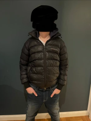 Svart dunjacka med huva Peak Performance - Säljer en svart dunjacka från Peak Performance med huva och dragkedja framtill. Jackan har ribbade muddar vid ärmsluten och justerbar huva. Två små hål på vänstra armbågen. Det ena är lagat. 