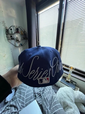 Blå LA Dodgers World Series keps - Snygg blå keps från New Era med LA Dodgers-logga framtill och World Series-märke på sidan. Baksidan har stor brodyr med texten 'World Series Champs' och MLB-logga. Klassisk 59FIFTY-modell med rak skärm och broderade detaljer. Perfekt för dig som gillar baseball och streetwear.