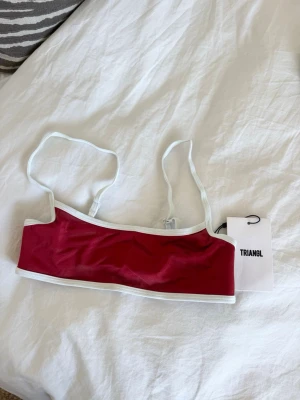 Oanvänd Röd bikiniöverdel från Triangl - Bikiniöverdel från Triangl i röd färg med vita kanter och smala axelband. Oanvänd med lappen kvar, stolen Small +