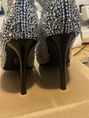 Steve Madden - Säljer ett par riktigt snygga stövletter täckta med glittrande strass. Skorna har spetsig tå och smal hög klack i svart. Perfekta för dig som vill sticka ut och älskar bling! Materialet är textil täckt med stenar och klacken är i lackad plast. Skorna är oanvända 