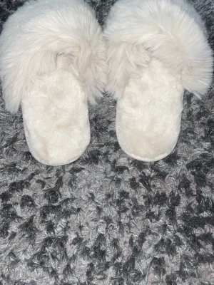 Vita fluffiga tofflor i storlek 36/37 - Supermjuka och fluffiga vita tofflor med bred pälskant och skön innersula. Perfekta att glida runt i hemma för en mysig känsla. Sula i gummi för extra grepp. Hör av er vid frågor eller intresse!
