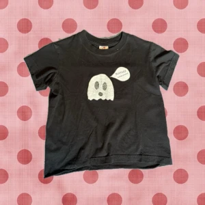 Svart t-shirt med spöke och text - Svart t-shirt med ett vitt spöke och pratbubbla med texten 'BUUUUH' tryckt på bröstet. T-shirten har rund hals, korta ärmar och en croppad passform. Perfekt för dig som gillar roliga och unika tryck.