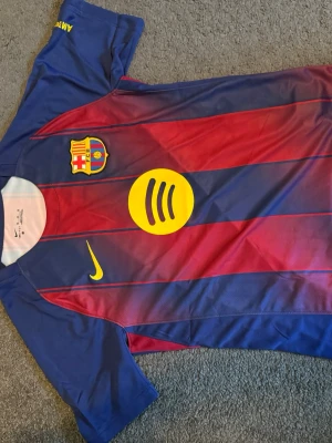 FC Barcelona matchtröja Nike - Säljer en FC Barcelona matchtröja från Nike i blått och rött med gula detaljer. Tröjan har klubbmärke, Nike-logga och sponsortryck på bröstet samt UNHCR-tryck på ryggen. Korta ärmar och sportig passform, perfekt för fotbollsträning eller match.