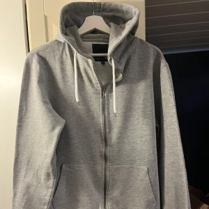Grå hoodie från 157 - Säljer en grå hoodie från 157 i storlek XL. Den har en dragkedja framtill och en mysig huva med snören. Perfekt för kyliga dagar med sin mjuka insida. Passar både till vardags och avslappnade tillfällen. Kan mötas upp i Sthlm/närförort å slippa fraktkostnaden. Djur/rökfritt hem. 