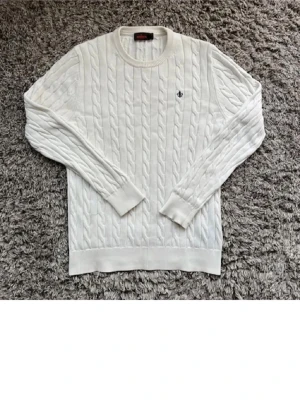 Vit kabelstickad tröja från Morris - Vit kabelstickad tröja från Morris med rund halsringning och diskret logga broderad på bröstet. Tröjan har långa ärmar och ribbade muddar vid ärmslut och nederkant. Perfekt för en stilren och klassisk look. Passar perfekt nu till våren och är de frågor så är de bara att skriva 