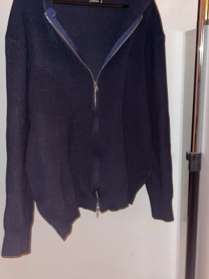 Mörkblå stickad hoodie med dragkedja - Mysig mörkblå stickad hoodie med dragkedja framtill och huva. Tröjan har långa ärmar och ribbade muddar vid ärmslut och nederkant. Perfekt för lager på lager och chill dagar. Bara att höra av dig vid fundering, pris kan diskuteras!✌🏼