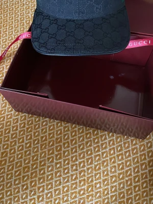 Svart keps från GG med monogram - Snygg svart keps från GG med klassiskt GG-monogram över hela kepsen. Kepsen har en böjd skärm och justerbart band bak i grönt och rött. Perfekt accessoar för att lyfta din streetwear-look.