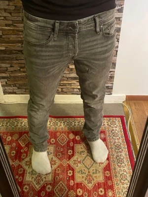 Grå slim fit jeans - Säljer ett par grå slim fit jeans med klassisk femficksdesign och dragkedjegylf. Jeansen har en snygg tvättad look och sitter tajt längs benen. Perfekta för dig som gillar en modern och stilren stil.