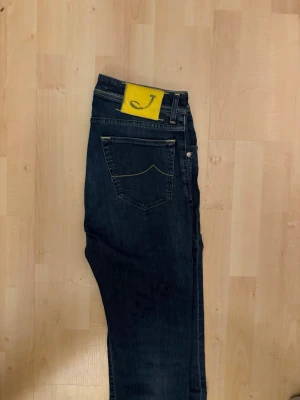 Mörkblå jeans från Jacob Cohen - Snygga mörkblå jeans från Jacob Cohen med raka ben och klassisk femficksmodell. Jeansen har en gul patch med ett J på bakfickan och är tillverkade i mjuk denim med subtila kontrastsömmar. Perfekta för en avslappnad men stilren look.
