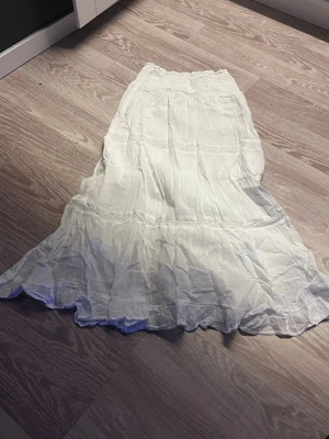 Vit långkjol från Gina Tricot - Luftig och flowy vit långkjol från Gina Tricot med resår i midjan och volangdetaljer. Perfekt för varma dagar och enkel att styla med både toppar och t-shirts.