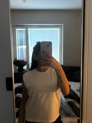 Vit ärmlös topp  - Säljer en enkel och stilren vit ärmlös topp från Designers, Remix som tyvärr inte kommer till användning längre och förtjänar en ny garderob. Toppen har en rak passform och rund halsringning, perfekt för att matcha med jeans eller shorts. Materialet är mjukt och känns skönt mot huden.